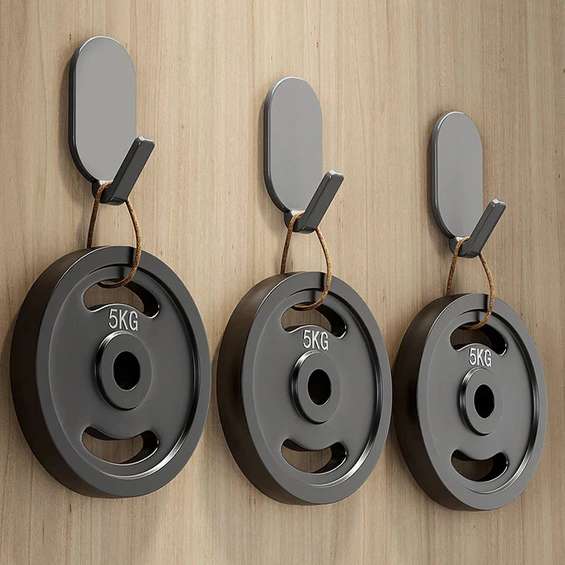 A set of three gray self-adhesive wall hooks with black mounting tabs displayed against a light wood background.