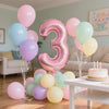 Un amas de ballons en papier alu rose et bleu clair formant le chiffre trois, décoré pour une célébration.
