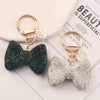 A pair of sparkling rhinestone bow keychains, one black and one silver, displayed on a white card.