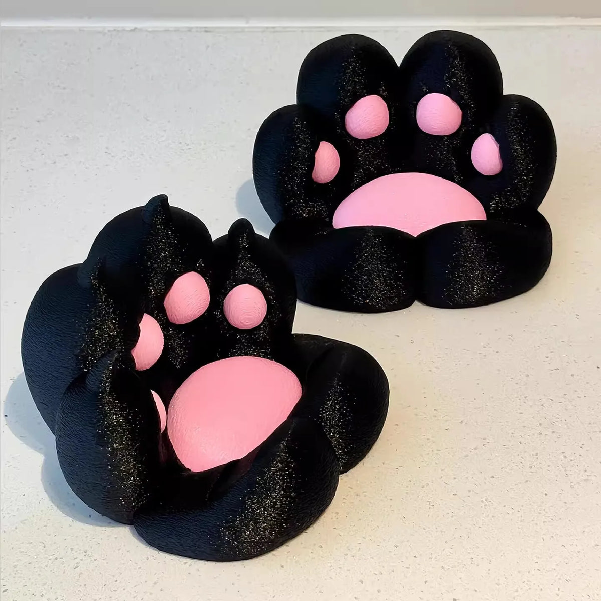 A pair of black silicone cat paw phone stands with pink accents, designed for stress relief.