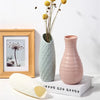 A pink textured vase holds dried yellow flowers next to a framed picture and a white ceramic object.