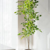 A tall artificial maple tree with silk green leaves in a gray planter, displayed indoors.