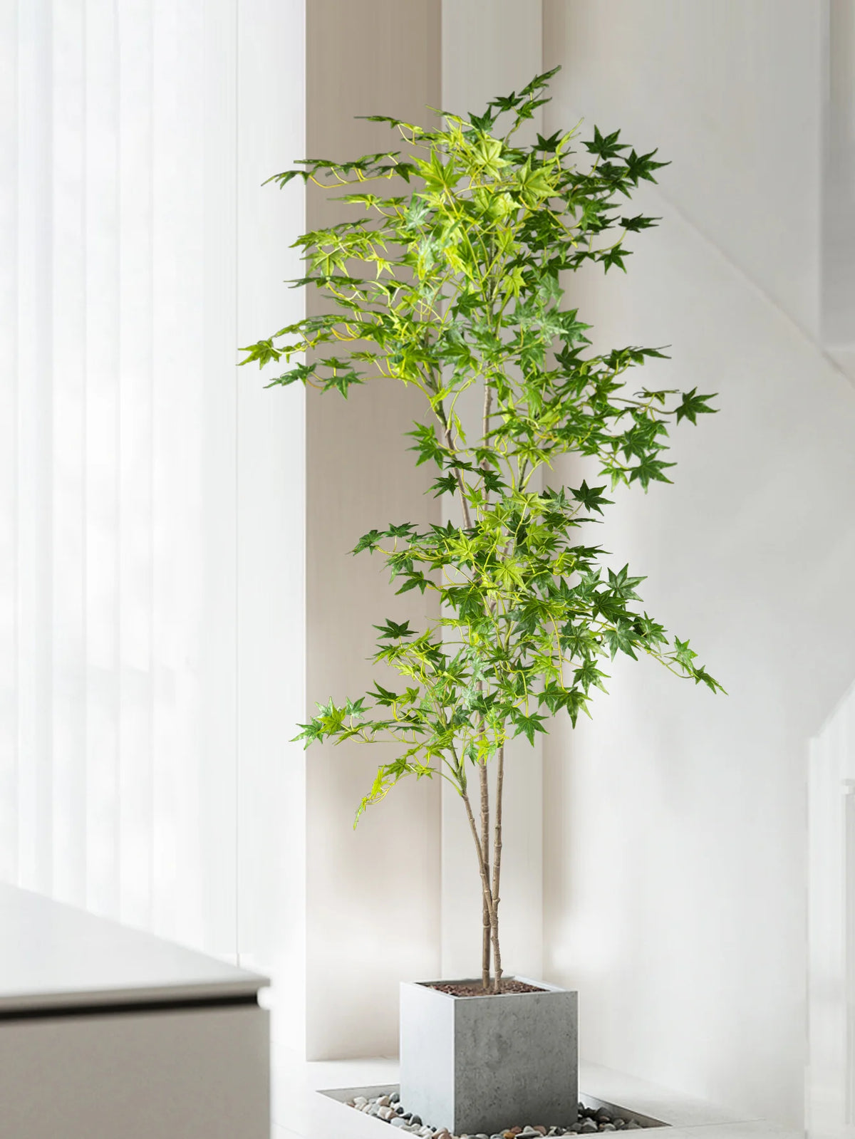 A tall artificial maple tree with silk green leaves in a gray planter, displayed indoors.