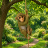 A small monkey figurine is hanging from a rope branch in a lush green garden setting.