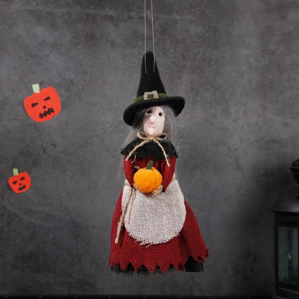 A witch ornament featuring a black pointed hat, gray hair, and a red dress with a straw apron, hanging against a dark gray ba