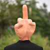 A hand with a middle finger extended, made of orange latex, against a blurred green outdoor background.
