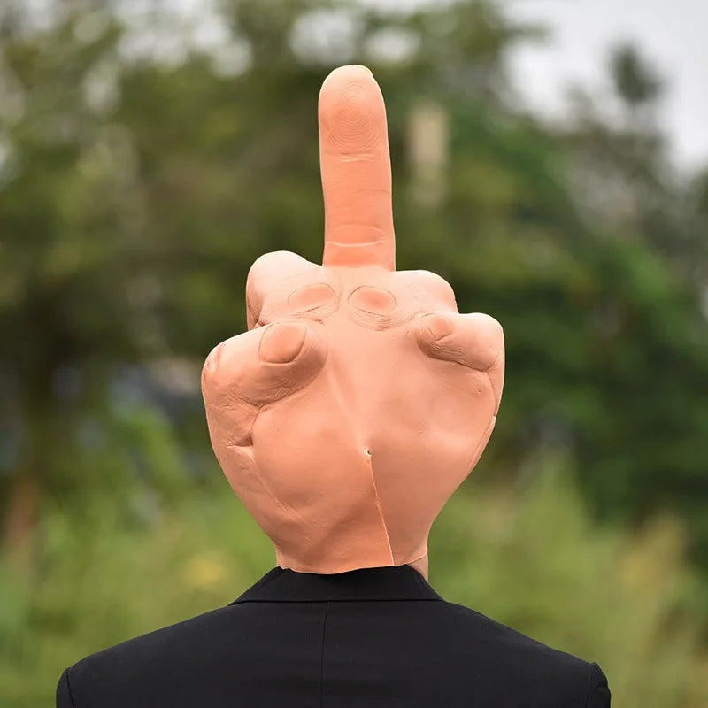 A hand with a middle finger extended, made of orange latex, against a blurred green outdoor background.