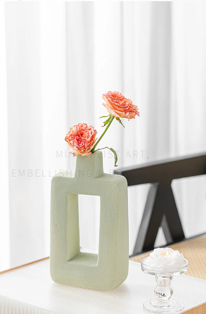A light green geometric ceramic vase holding a single pink rose in a bright, minimalist setting.