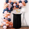 A black cocktail table draped with a stretch spandex tablecloth featuring a skirt, surrounded by balloons and a cake.