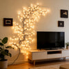 A decorative branch of willow-like LED lights illuminates a modern television setup on a wooden cabinet.