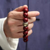 A hand holds a natural cinnabar stone zodiac bracelet with round red beads and a silver charm.
