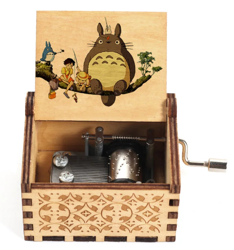 A hand-cranked wooden music box featuring a Totoro design, with an illustration of two children and a large cat on the lid.