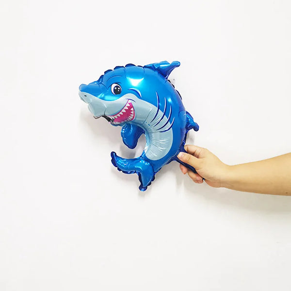 A hand holds a blue foil balloon shaped like a shark for party decor.
