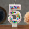 A white birthday candle shaped like the number 5 decorated with colorful candy beads.