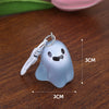 A light blue ghost-shaped keychain with a smiling face resting on a wooden surface.