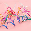 Colorful glitter curling ribbon rolls in various shades of pink, yellow, green, and blue scattered on a light background.