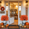 A display of artificial orange baby's breath flowers and pumpkins arranged on a porch with wooden doors.