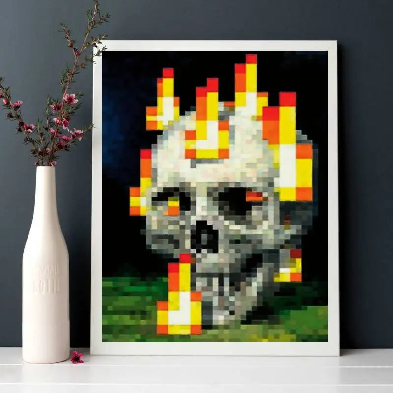 A framed pixel art print depicting a skull engulfed in bright orange and yellow flames against a dark background.