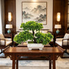 A potted artificial bonsai tree decoration sits on a dark wooden table in a traditional interior setting.
