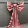 A large dusty rose satin bow with long tulle drapes hanging against a gray wall.