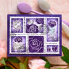 A purple postage stamp set featuring floral designs and words on a square card with pink flowers in the background.