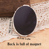 A black oval fridge magnet with a white decorative edge is shown resting on a beige surface.