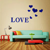 A wall decorated with blue heart stickers spelling the word LOVE above a teal sofa and a red coffee table.