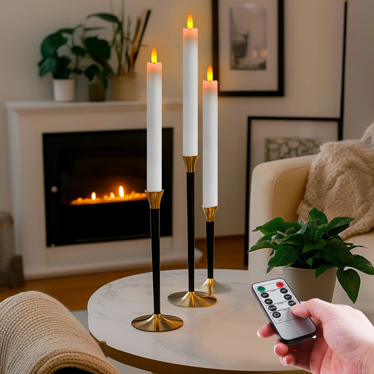 A hand holds a remote control for flameless LED taper candles placed on a table next to lit white candles.