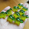 A hand holds several bright yellow and green glow-in-the-dark resin frog ornaments.