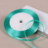 A spool of teal satin ribbon is shown on a white background.