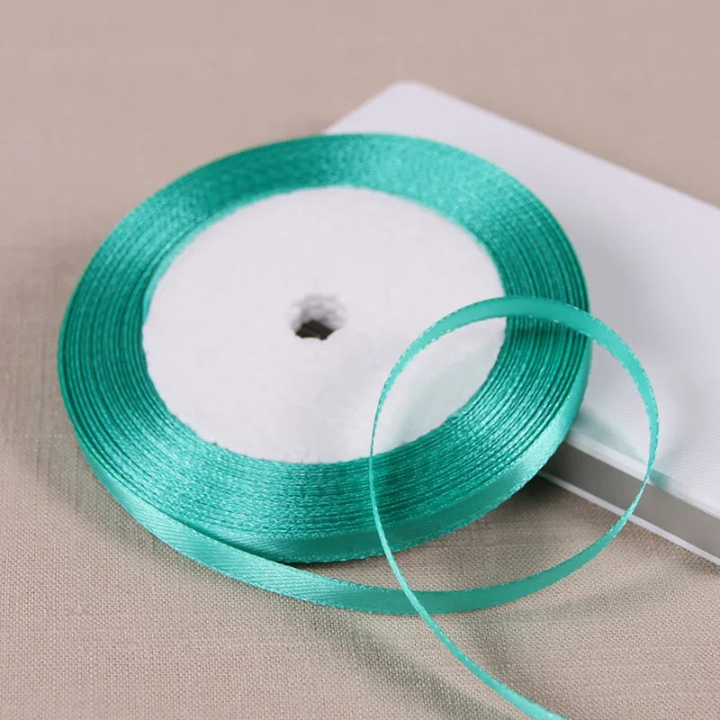 A spool of teal satin ribbon is shown on a white background.