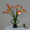 A bouquet of orange and peach artificial calla lily stems in a clear glass vase