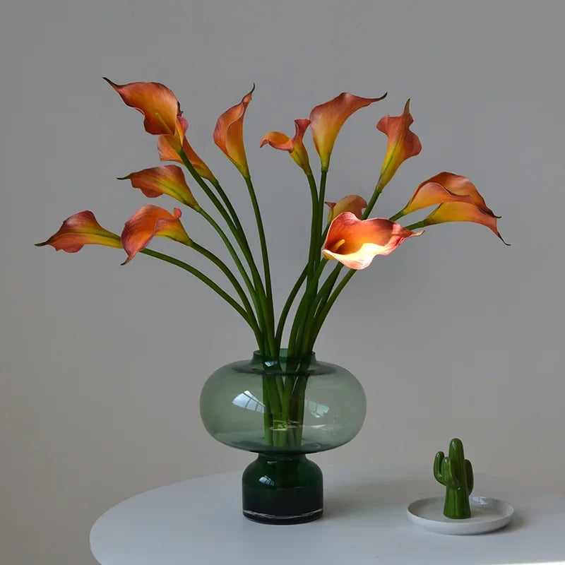 A bouquet of orange and peach artificial calla lily stems in a clear glass vase