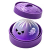 A purple silicone fidget dumpling with a ghost face design is shown inside its matching purple container.