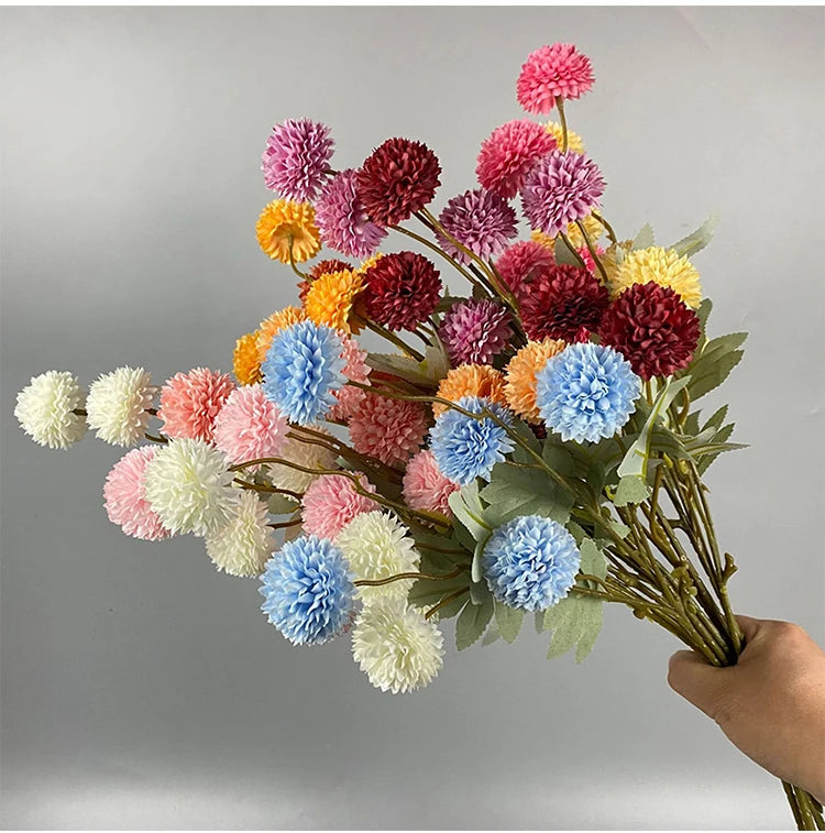 Un ramo de flores artificiales de crisantemo y diente de león en tonos rosa, púrpura, amarillo y azul.
