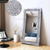 A tall silver crystal rhinestone wall mirror with a sparkling frame reflecting a bedroom interior.