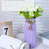 A purple plastic vase holds a bouquet of white flowers, decorated with twine, on a white marble surface.