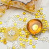 A collection of yellow and clear wax sealing beads scattered on a white surface next to a small gold-colored container.