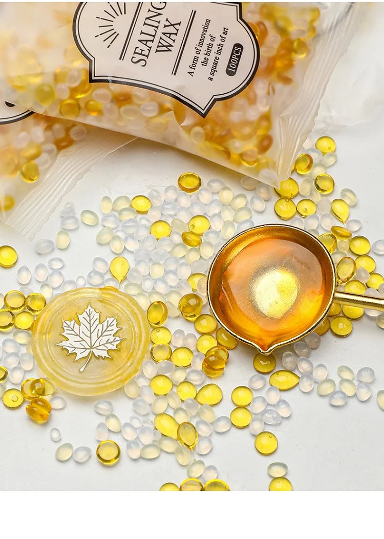 A collection of yellow and clear wax sealing beads scattered on a white surface next to a small gold-colored container.