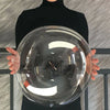 A person holds a large clear balloon reflecting light and surroundings against a gray textured background.