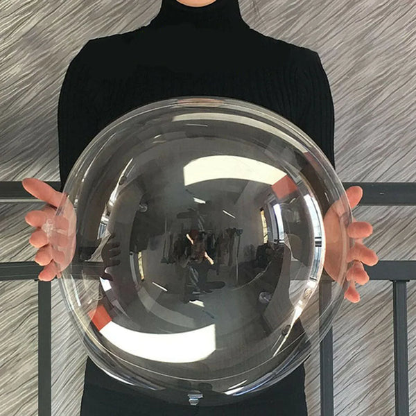 A person holds a large clear balloon reflecting light and surroundings against a gray textured background.