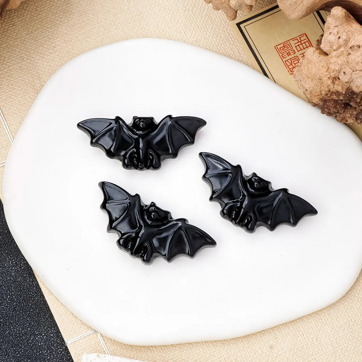 Three black hand-carved obsidian bat figurines displayed on a white ceramic plate.