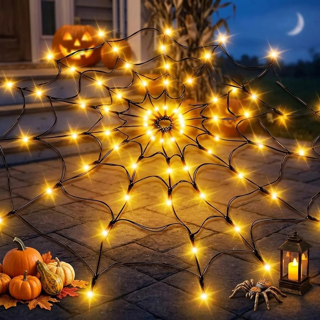 A glowing orange Halloween spider web made of LED string lights on a stone path with pumpkins and a spider.