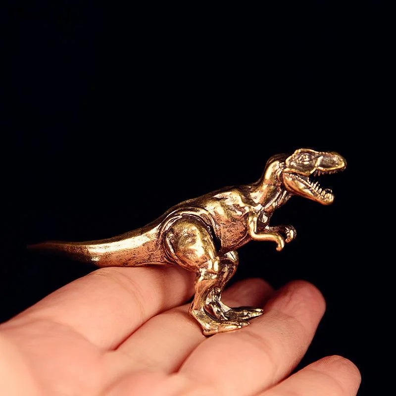 Ornement de dinosaure en laiton massif posé sur la paume d'une main, fond sombre.