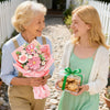 A smiling elderly woman and a young woman standing outdoors, holding a bouquet of pink faux flowers.