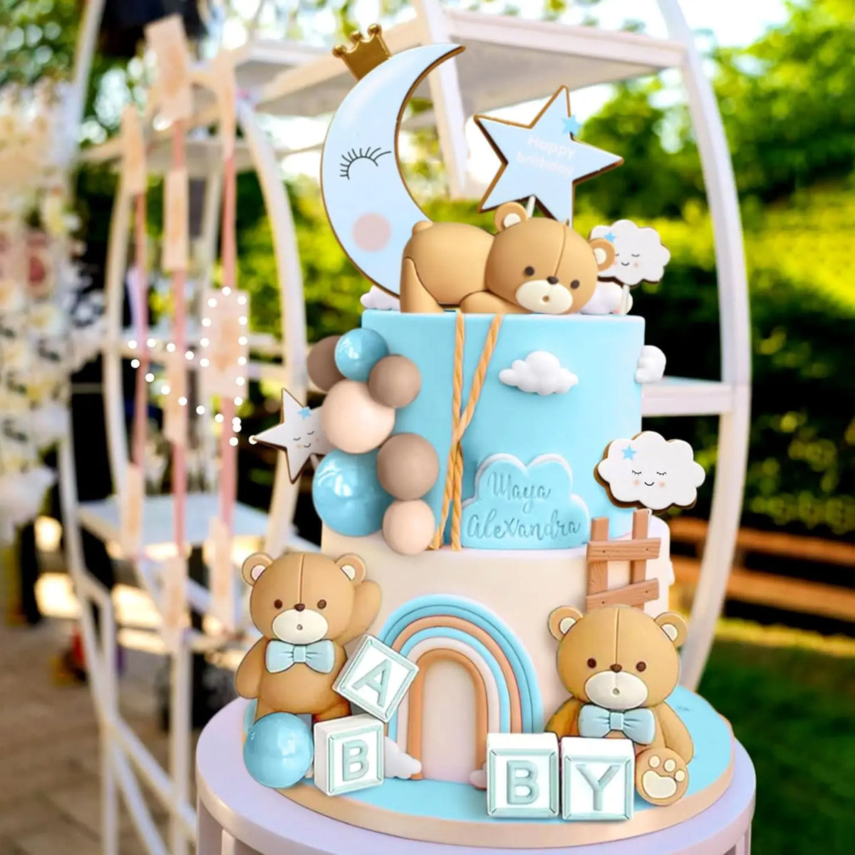 A tiered baby shower cake featuring bear figures, stars, clouds, and blue accents.