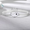 A white braided bracelet set featuring a yin-yang charm is displayed on a light surface.