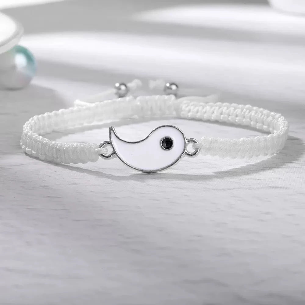 A white braided bracelet set featuring a yin-yang charm is displayed on a light surface.