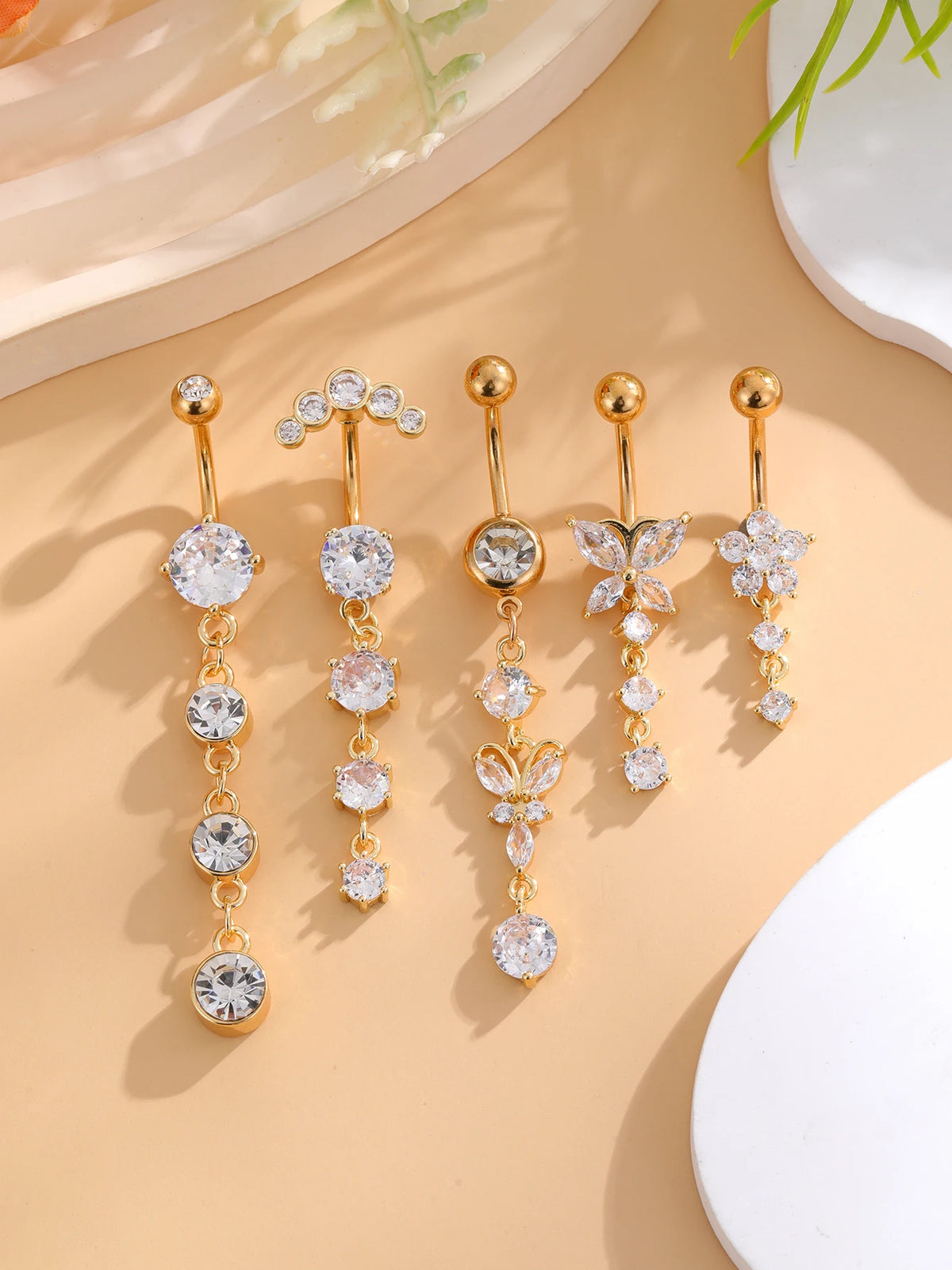 A set of five gold tone butterfly and flower belly rings displayed on a light beige background.