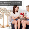Two women are presenting a gift box wrapped in red ribbon to each other, with elegant metal glass candle holders visible.